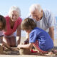 Two grandparents kneel on the beach making sandcastles with two grandchildren